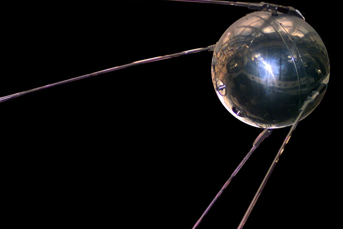 A polished metal sphere with four long antennas against a black background.