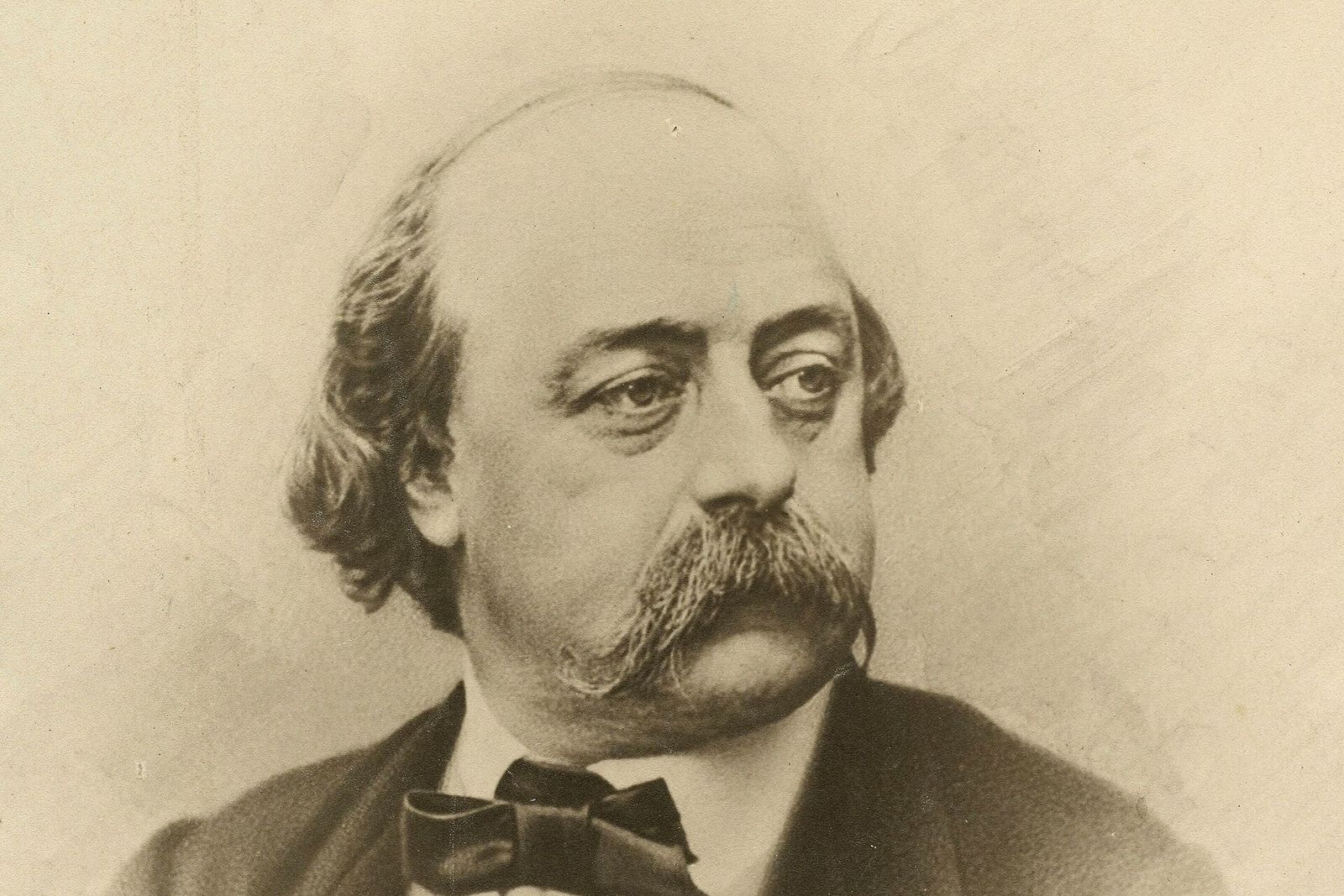Sepia portrait photograph of the novelist Gustave Flaubert, balding with a large moustache and bow tie.