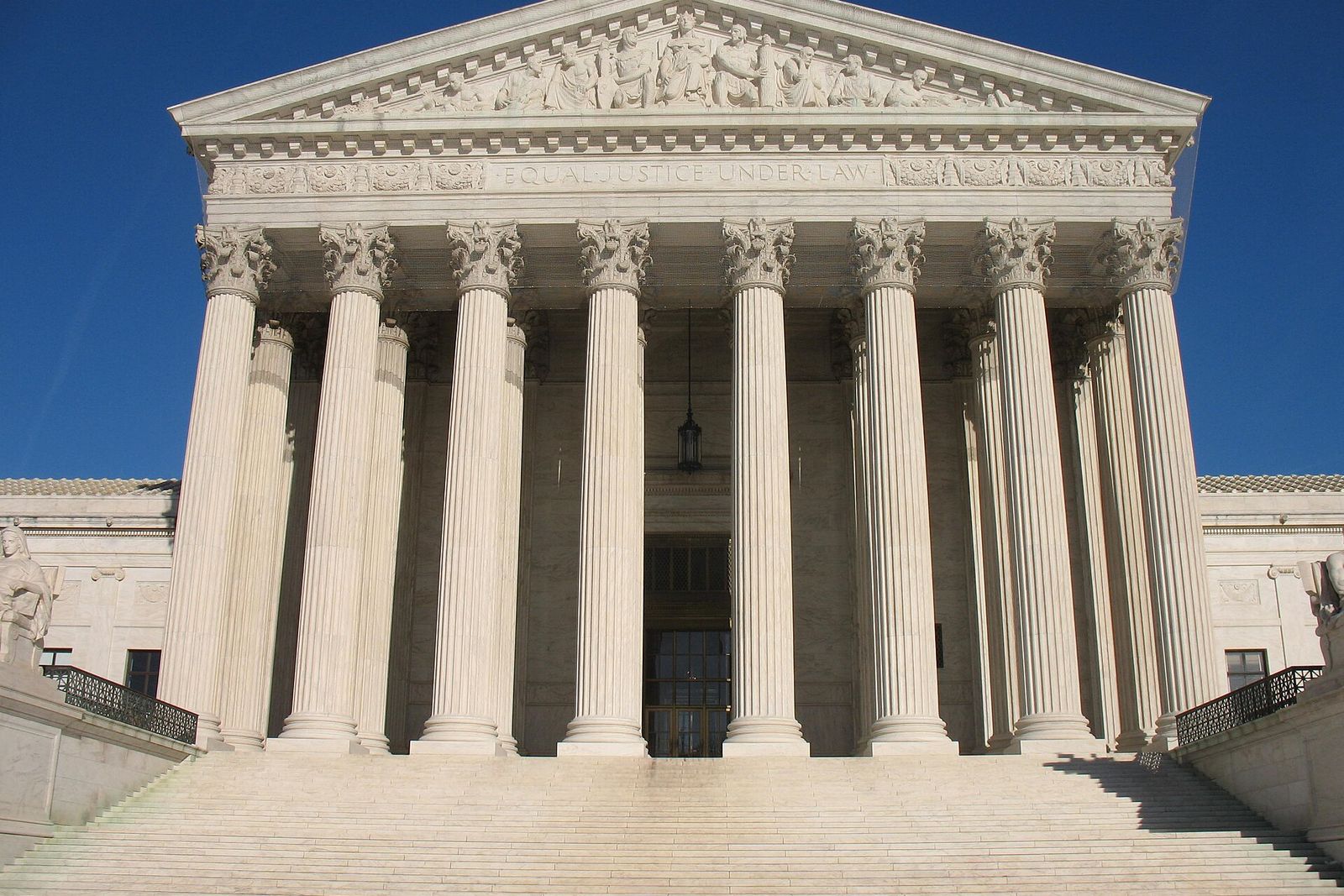 The columned west facade and steps of the United States Supreme Court building under a blue sky.