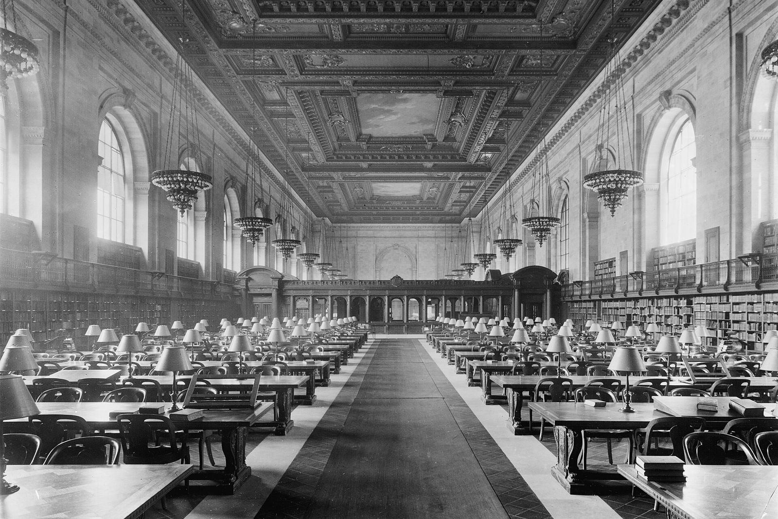 Readers at long tables under the high windows and chandeliers of a vast library reading room.