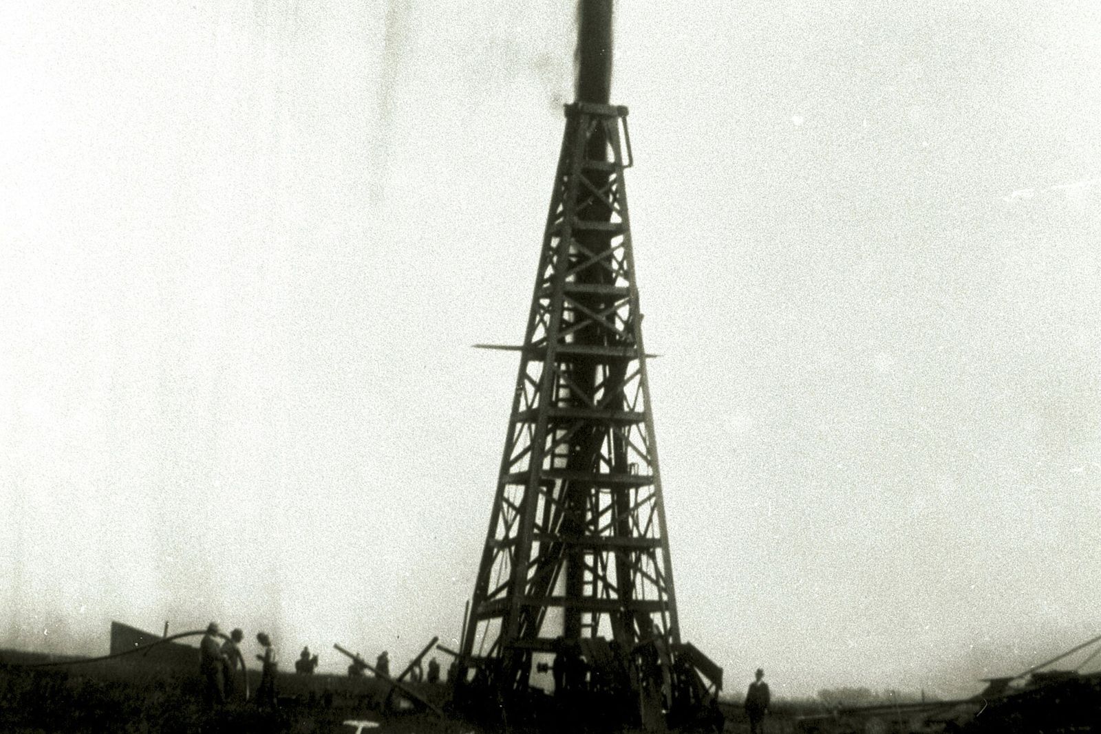 A black column of oil spouting high above a wooden derrick on the Texas plain.