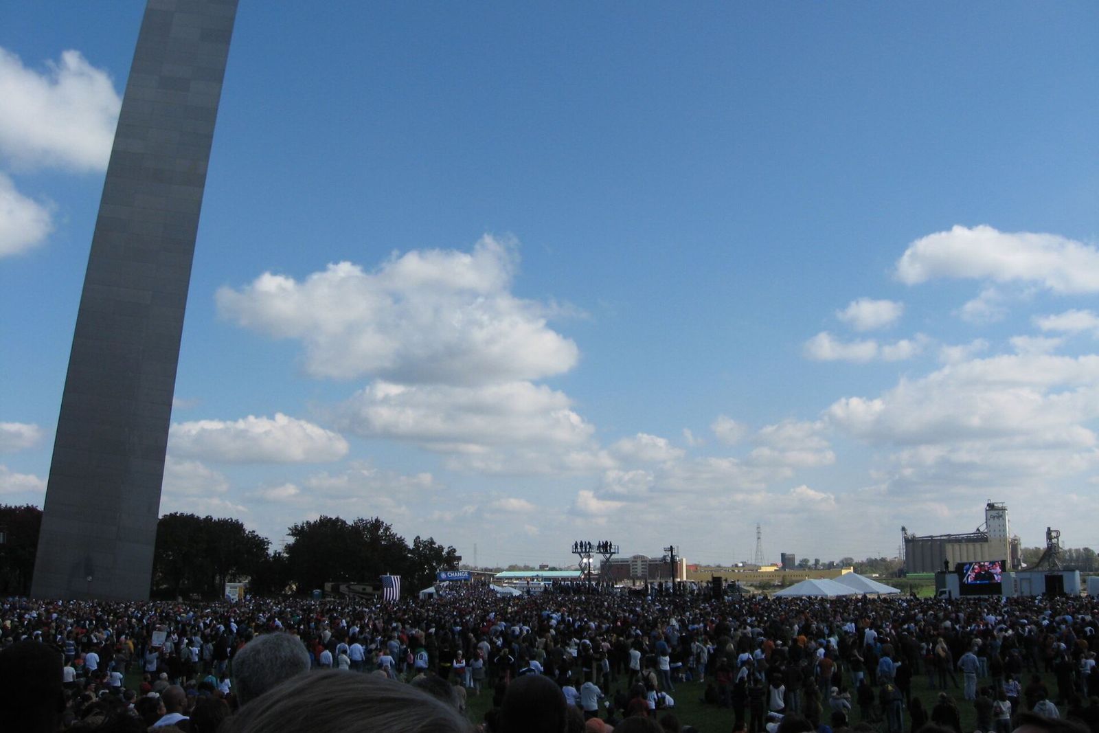 A huge crowd fills a park beneath the Gateway Arch at a campaign rally.