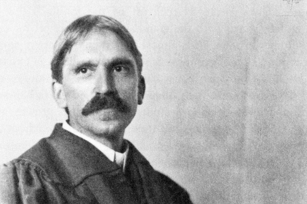 Portrait of John Dewey in academic robes, seated and looking toward the camera.