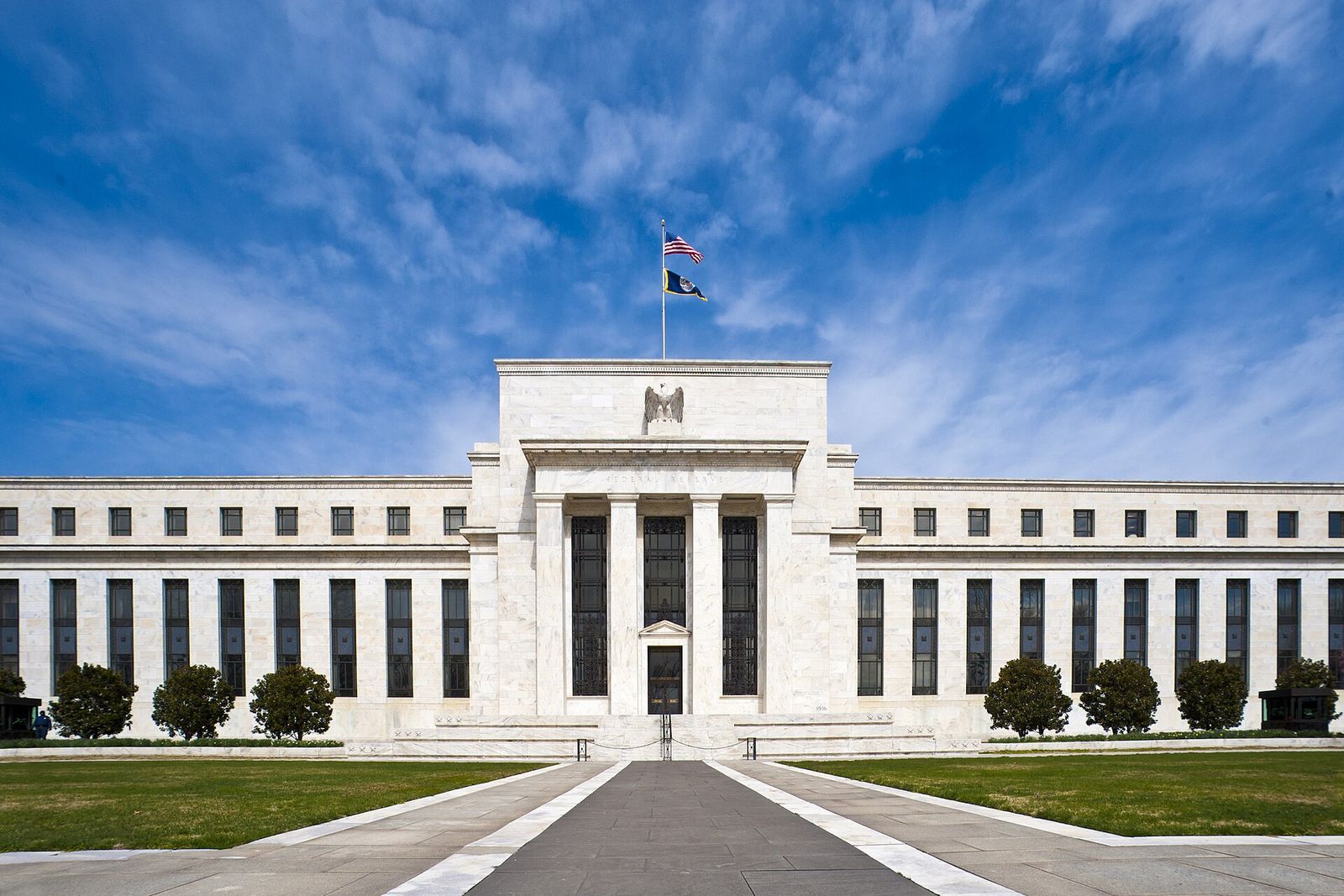 The white marble front of the Eccles Building under a blue sky, with the American flag above its entrance.