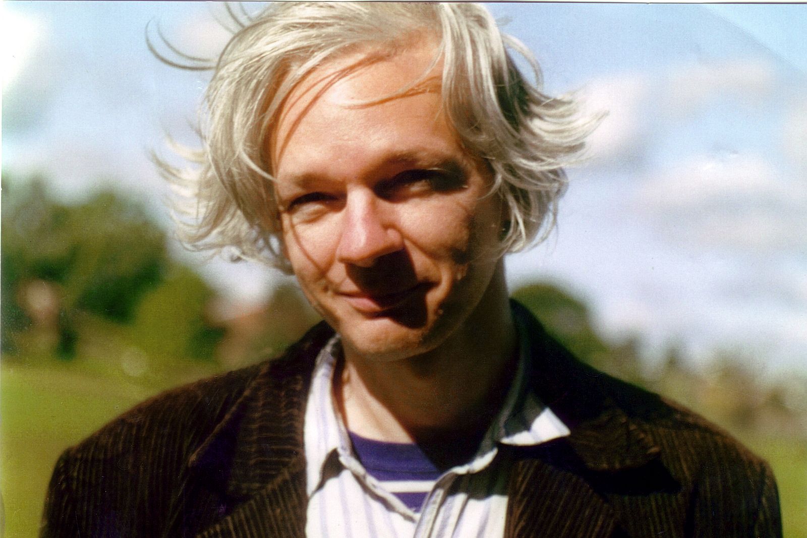 Portrait of Julian Assange outdoors with wind-blown pale hair.