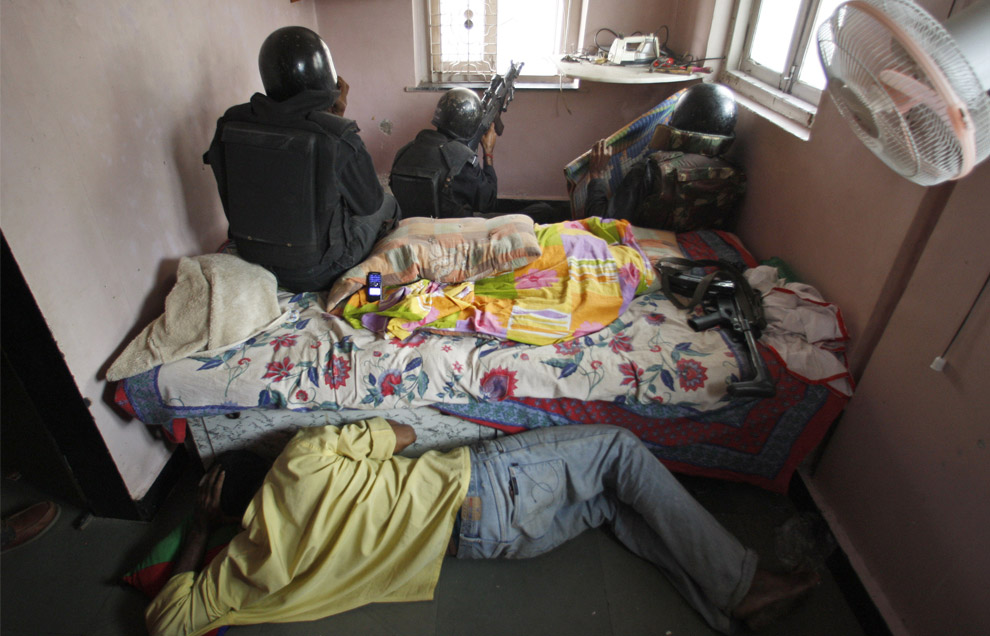 A resident takes cover for possible return fire as National Security Guard commandoes fire at suspected militants holed up at Nariman House in Colaba, Mumbai, India, Friday, Nov. 28, 2008.